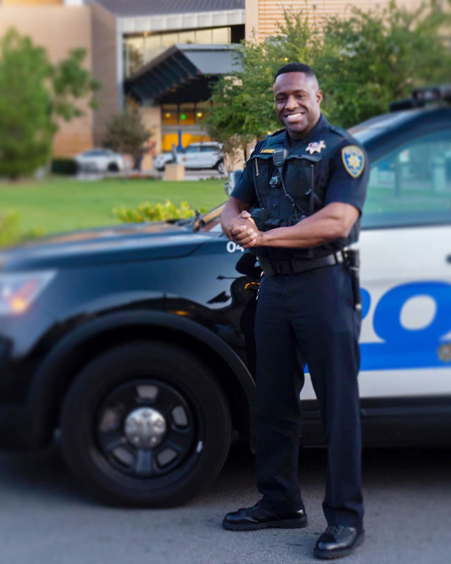 police officer smiling standing next to police car